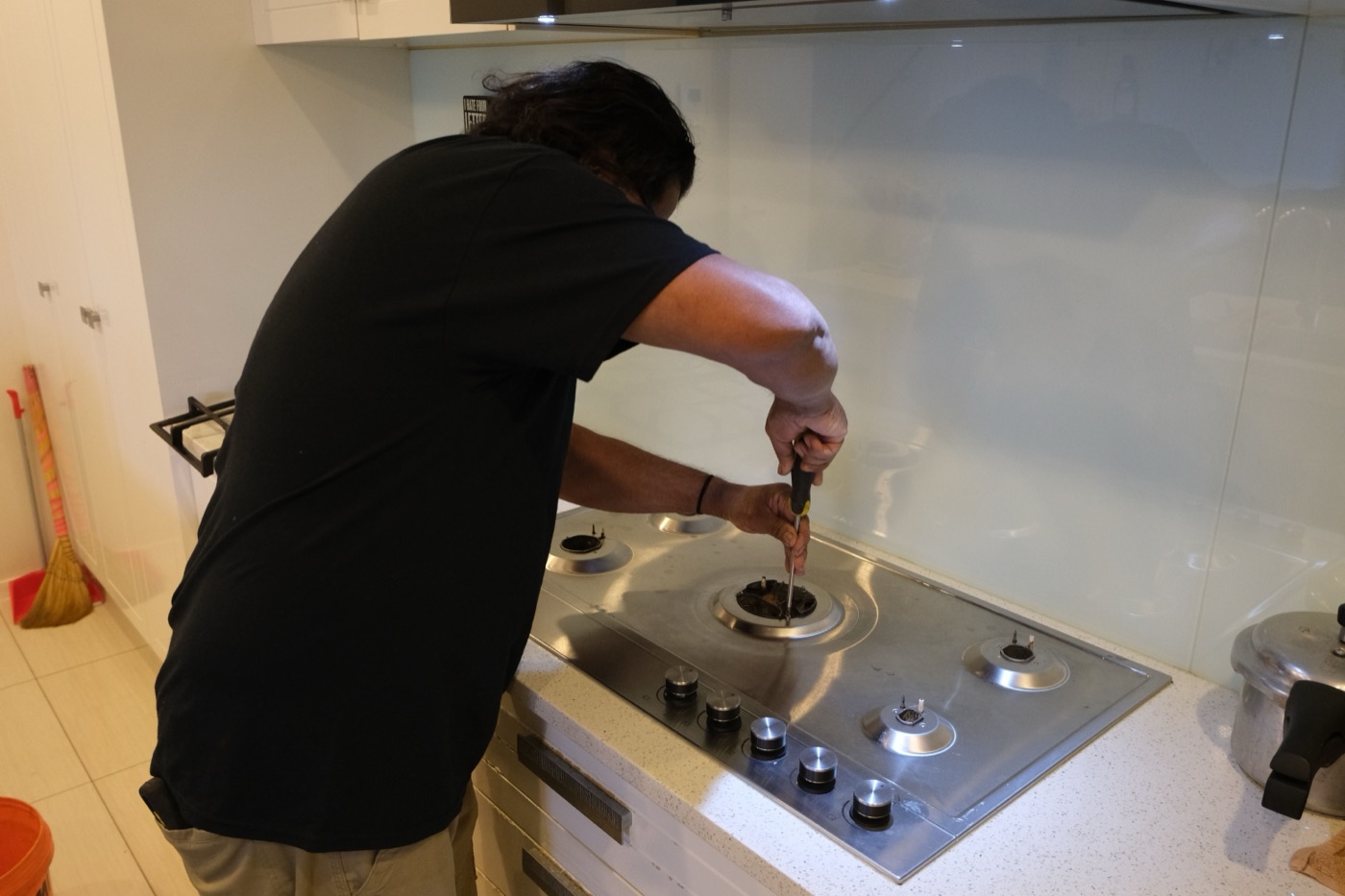 Savio repairing a gas cooktop burner in a kitchen