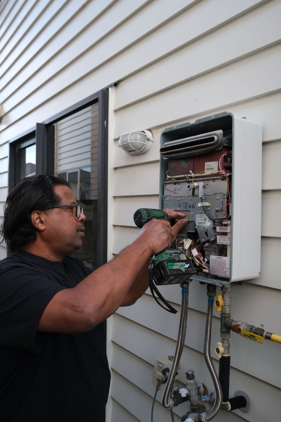 Savio installing a gas hot water unit on an exterior wall
