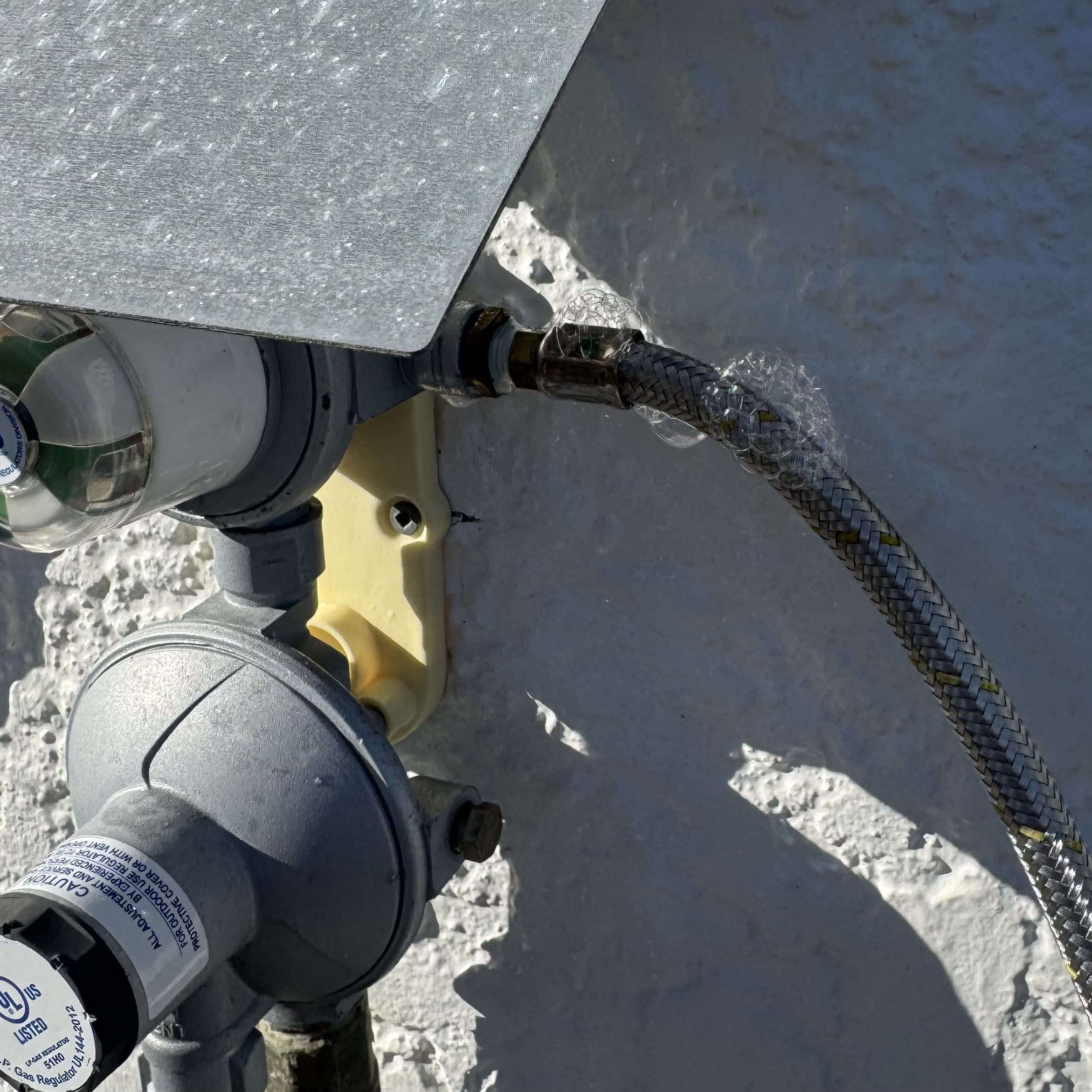 Gas regulator and braided connection hose fitted on an exterior wall by Fernz Gas & Plumbing Specialist